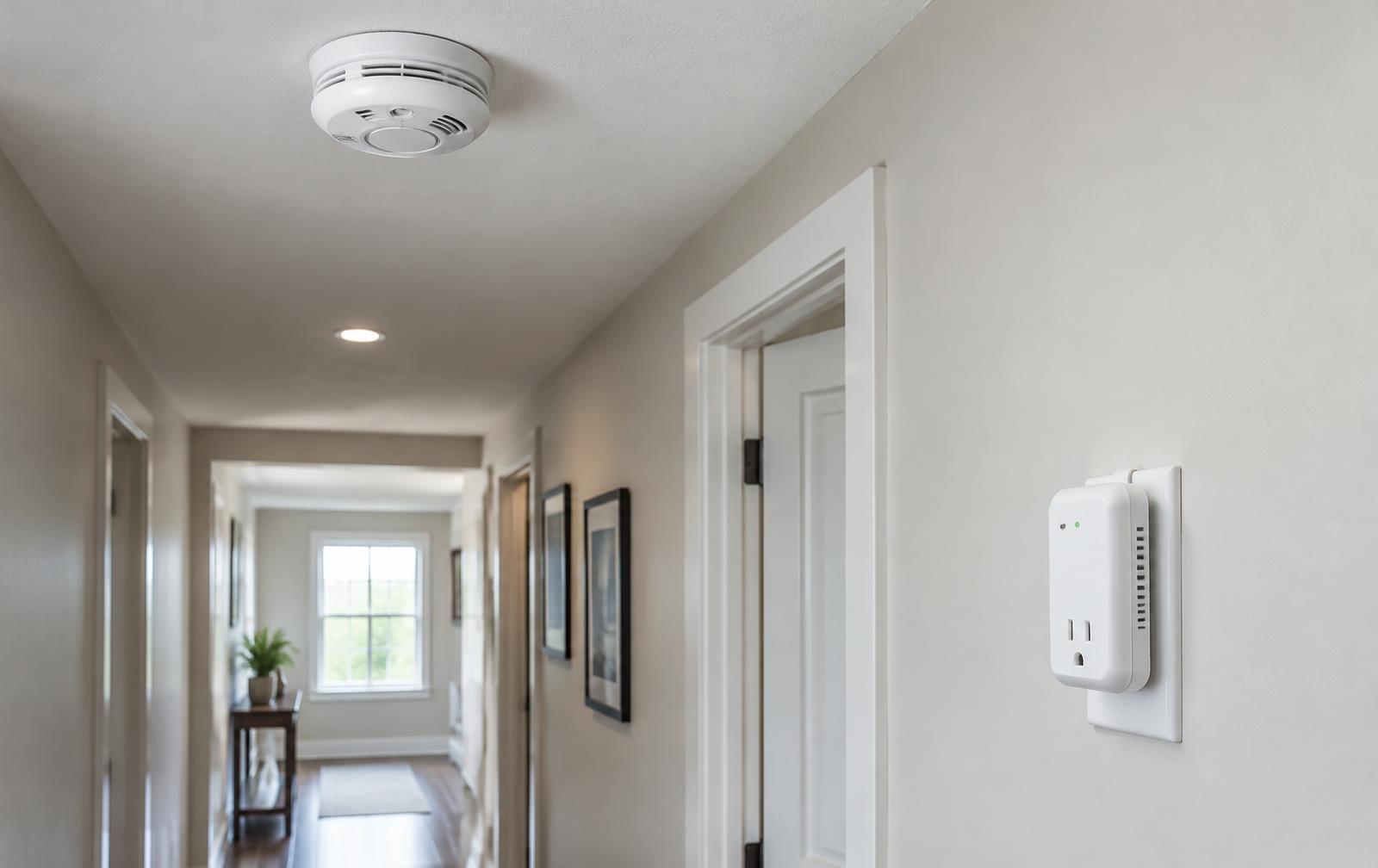 Ceiling smoke detector and wall surge protector installed in a home hallway